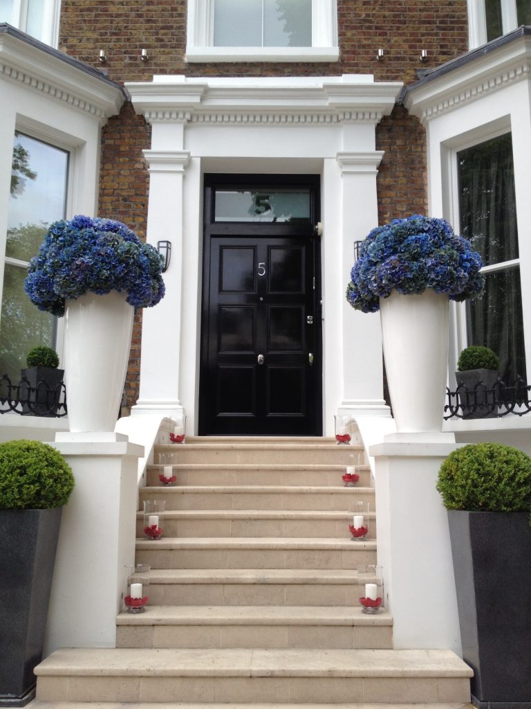 Tall white planters of blue hydrangeas framing an entrance, with candles along the steps